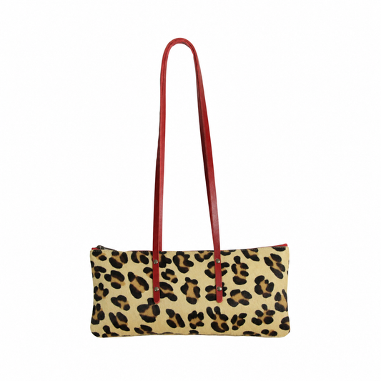 Sac Le Baguette en cuir à poils, motif léopard, avec ses anses rouges fixées sur la face du sac, vu de face sur fond blanc.